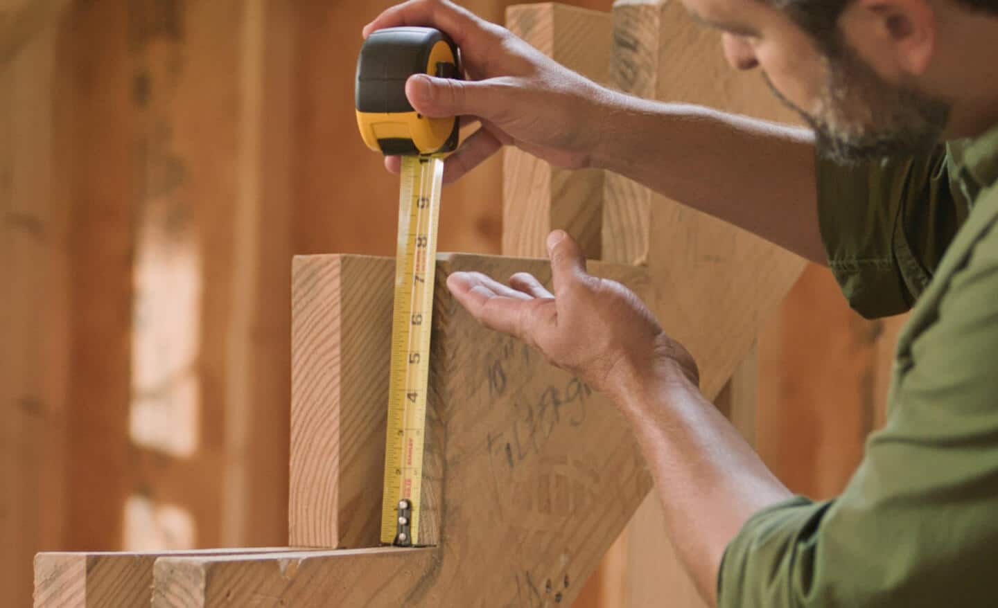 A Pro measures the rise of a stair stringer with a tape measure.