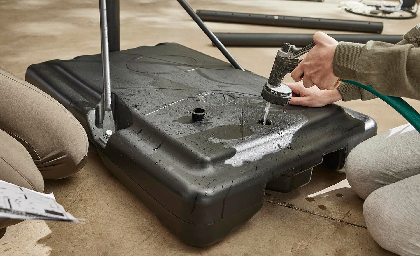 Someone adding water to the base of a portable basketball hoop.