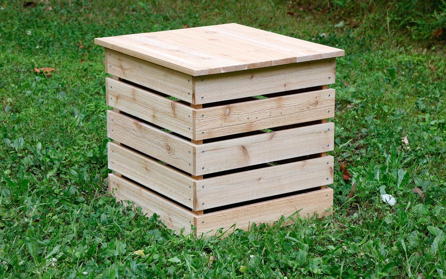 A wooden DIY compost bin sitting in the grass.
