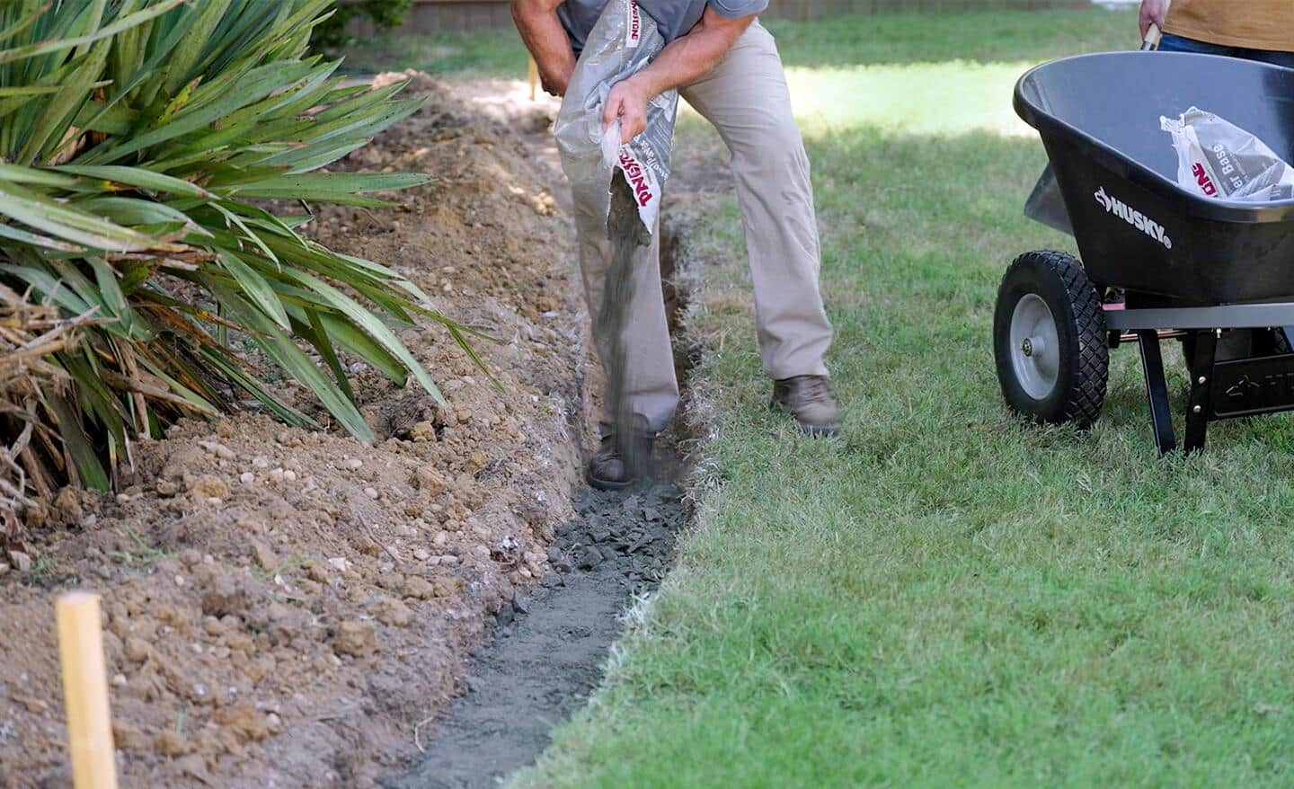 A paver base, consisting primarily of finely grushed gravel, is poured into the trench foundation of a retaining wall.