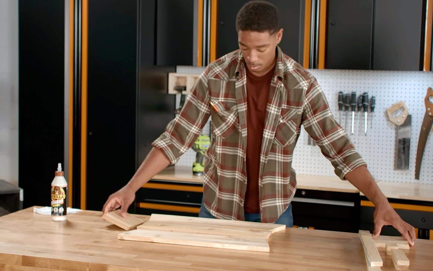 An individual lays out multiple wooden pieces on a table to assemble a window box.  