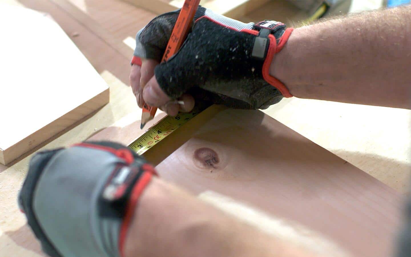 A person using a pencil and a tape measure to mark a board's bottom edge.