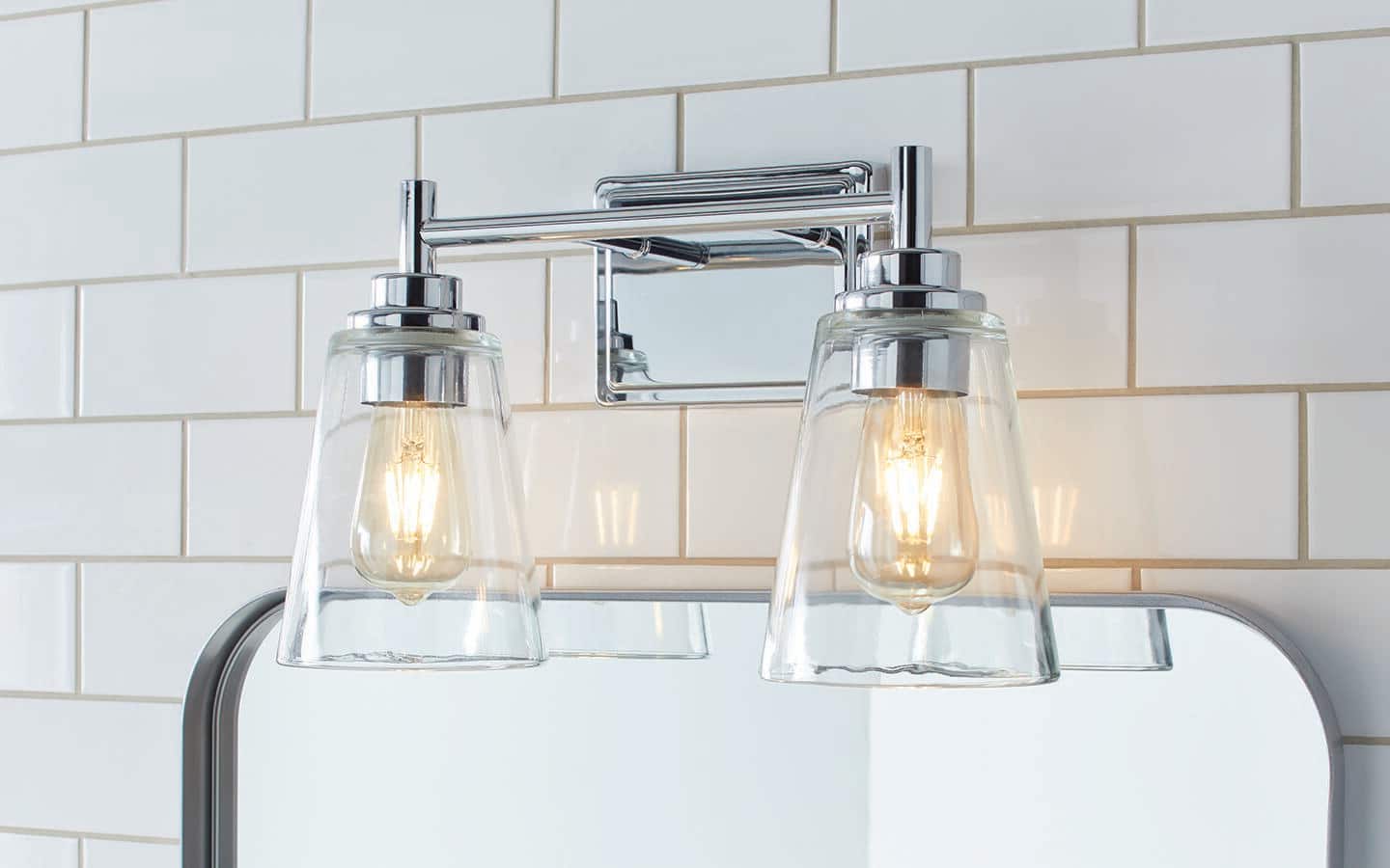 A vanity light bar featuring two lamp fixtures with glass shades hangs above a bathroom mirror. A vanity light bar featuring two lamp fixtures with glass shades hangs above a bathroom mirror.