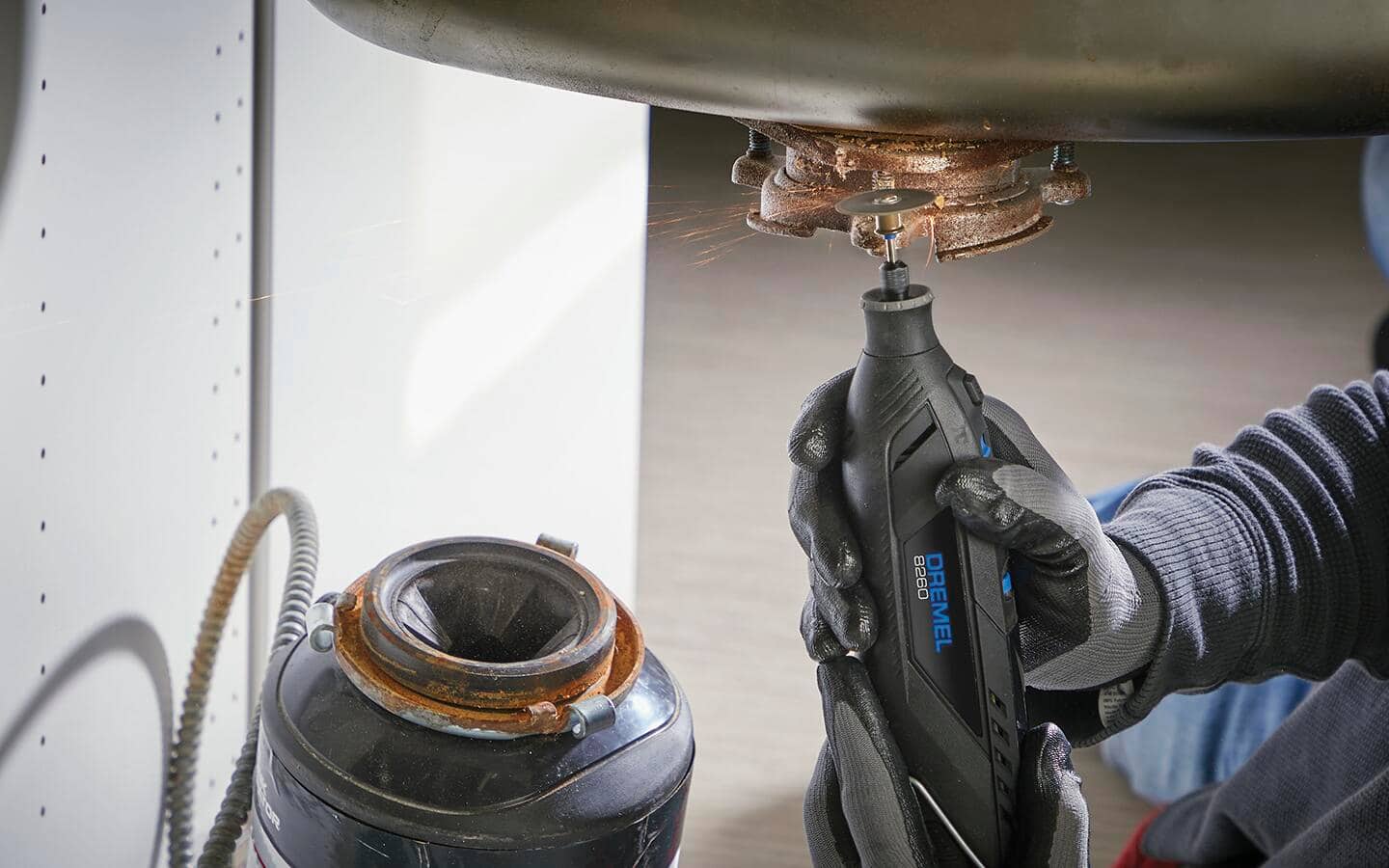 Someone wearing work gloves using a rotary tool to clean a drain. Someone wearing work gloves using a rotary tool to clean a drain.