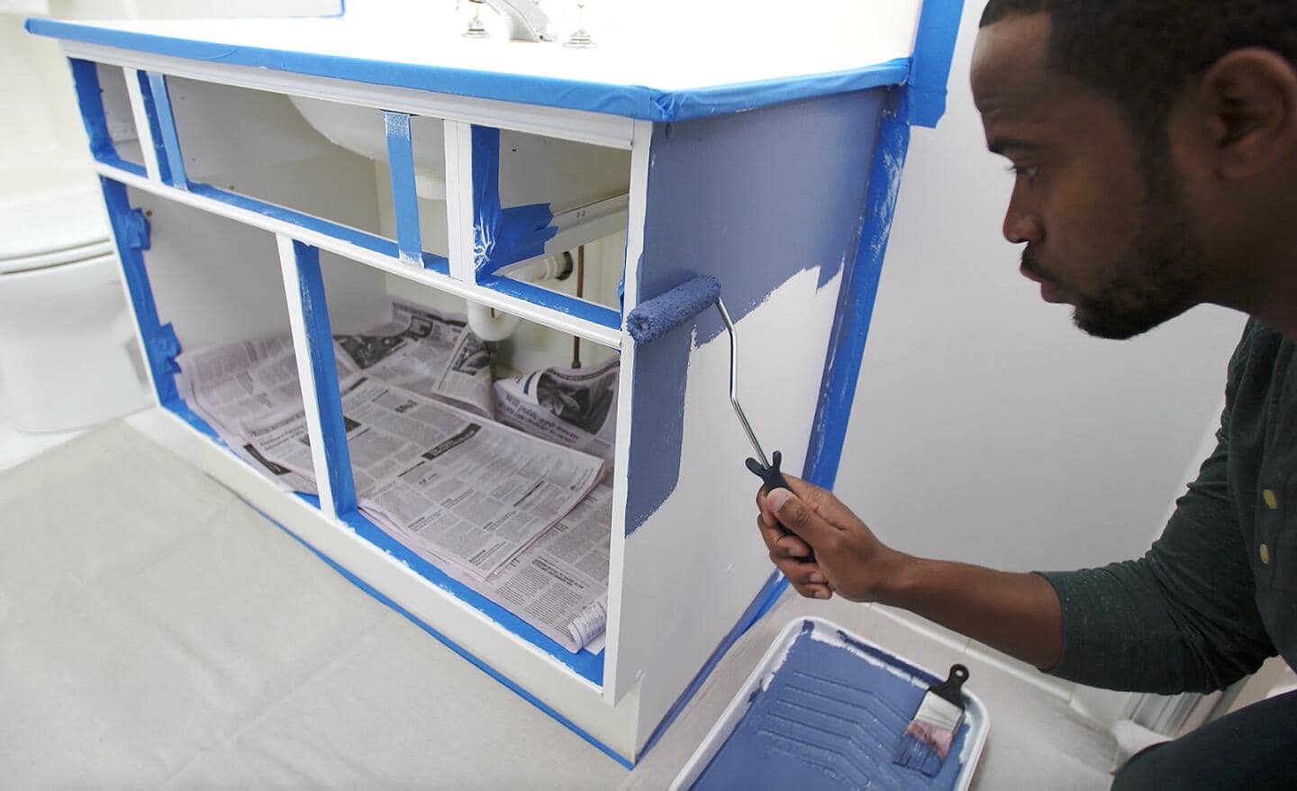 A person applying blue paint to a bath vanity with a paint roller.