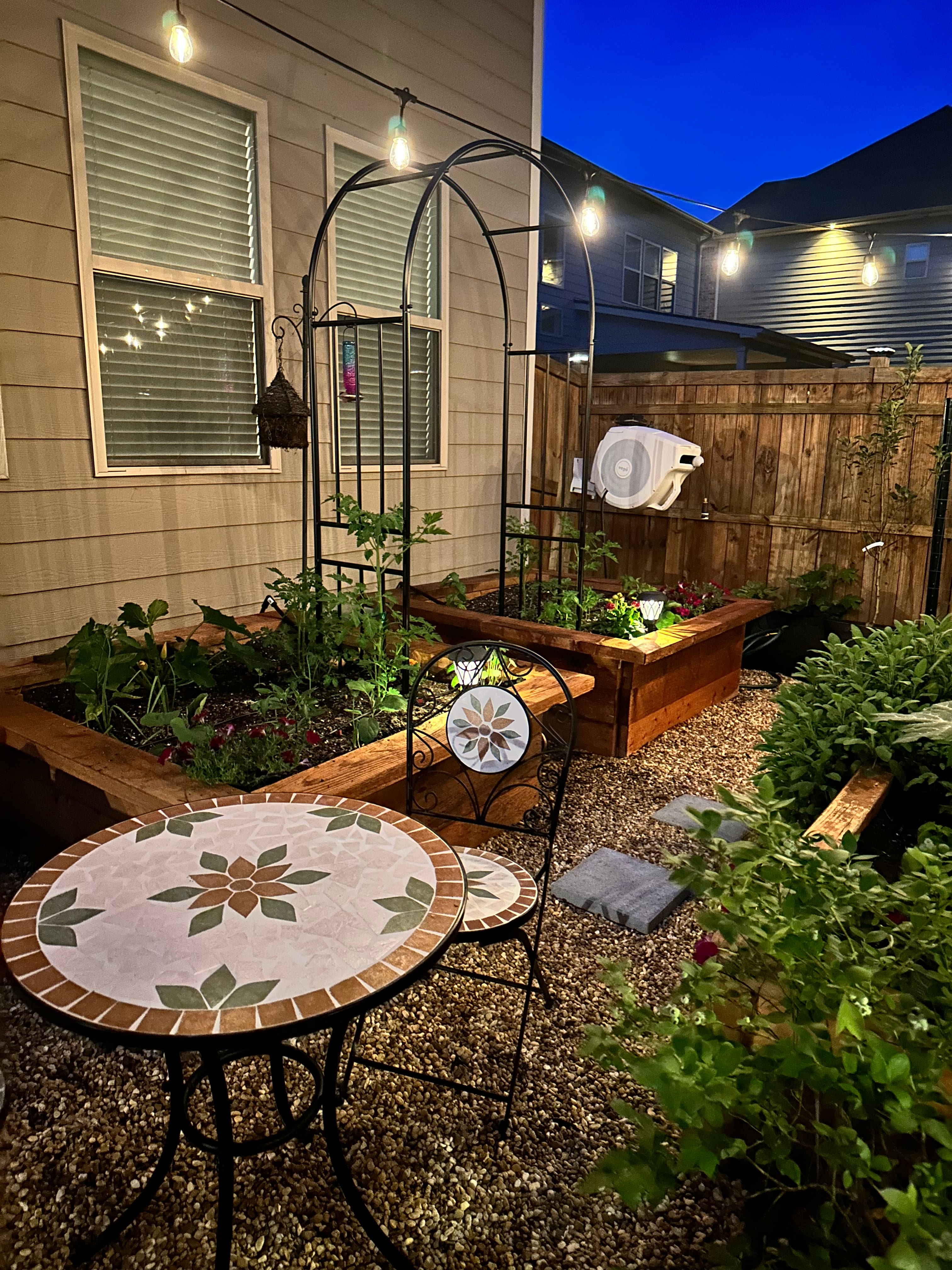 An evening look at a revamped backyard space featuring raised garden beds, trellis, and bistro set. An evening look at a revamped backyard space featuring raised garden beds, trellis, and bistro set.