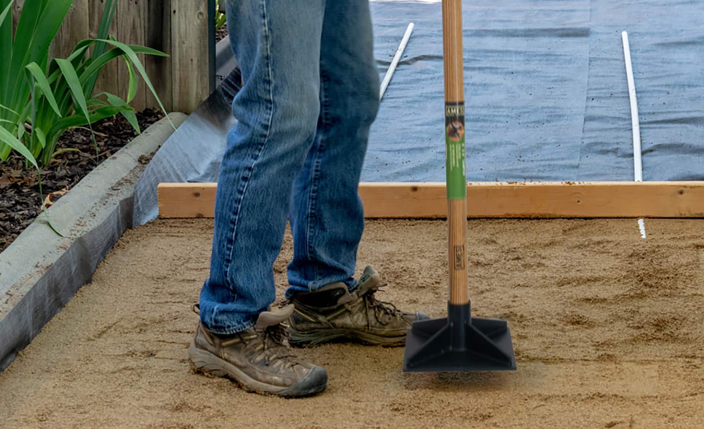 A person tamps gravel with a tamper.