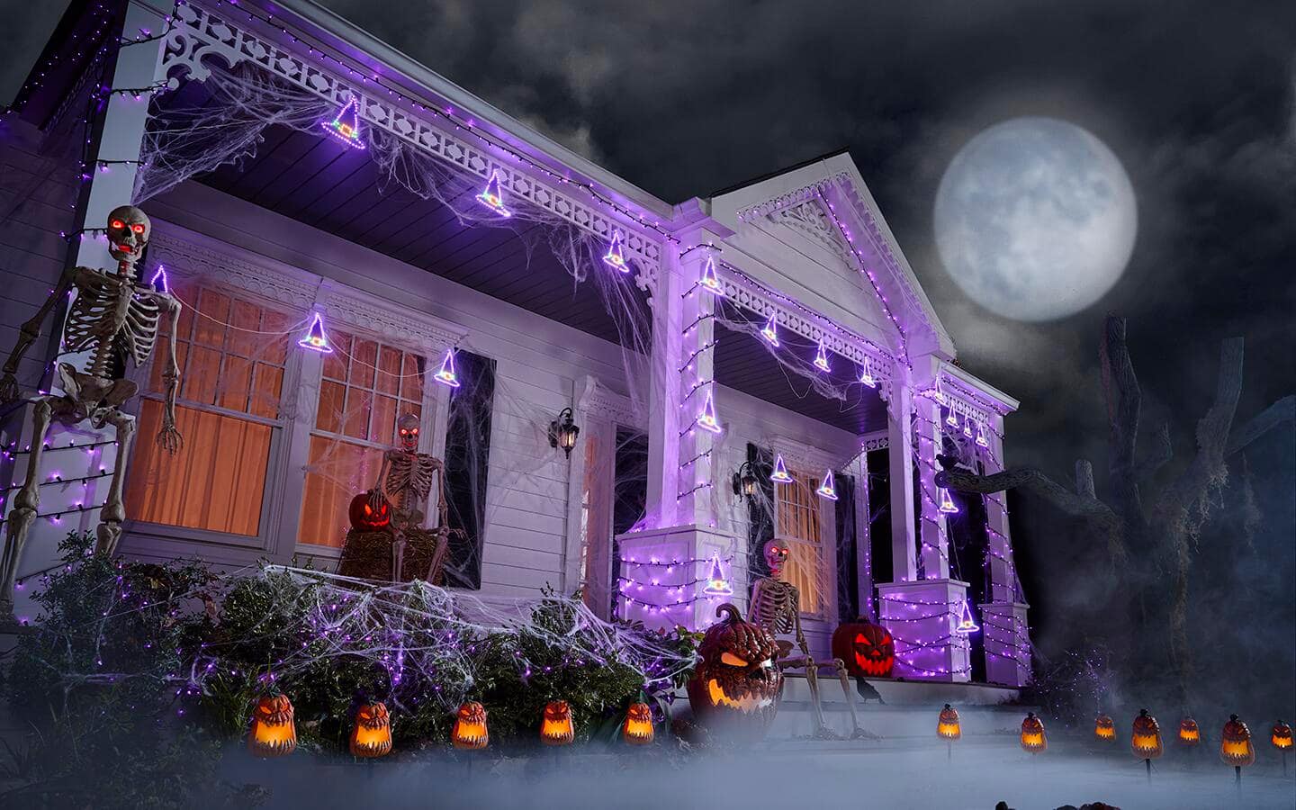 Purple string lights and lighted jack-o'-lanterns and skeletons decorate a front porch for Halloween. Purple string lights and lighted jack-o'-lanterns and skeletons decorate a front porch for Halloween.