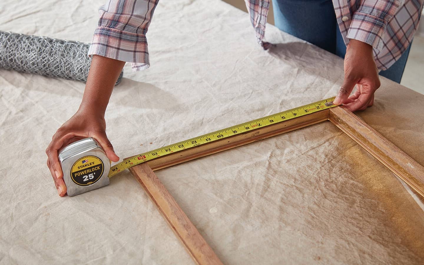 A person measures a frame with a tape measure. A person measures a frame with a tape measure.