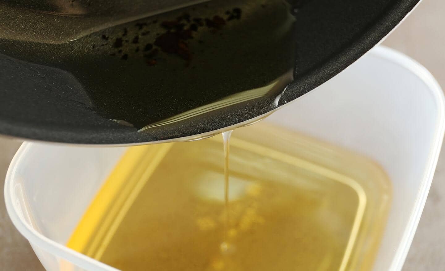 Oil is poured from a frying pan into a container.