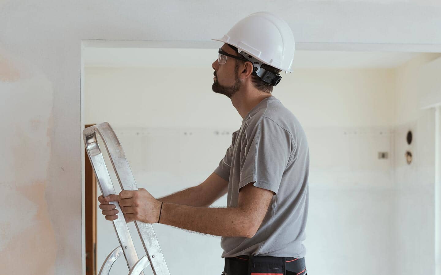 A man wearing a hardhat and safety glasses climbs a ladder. A man wearing a hardhat and safety glasses climbs a ladder.