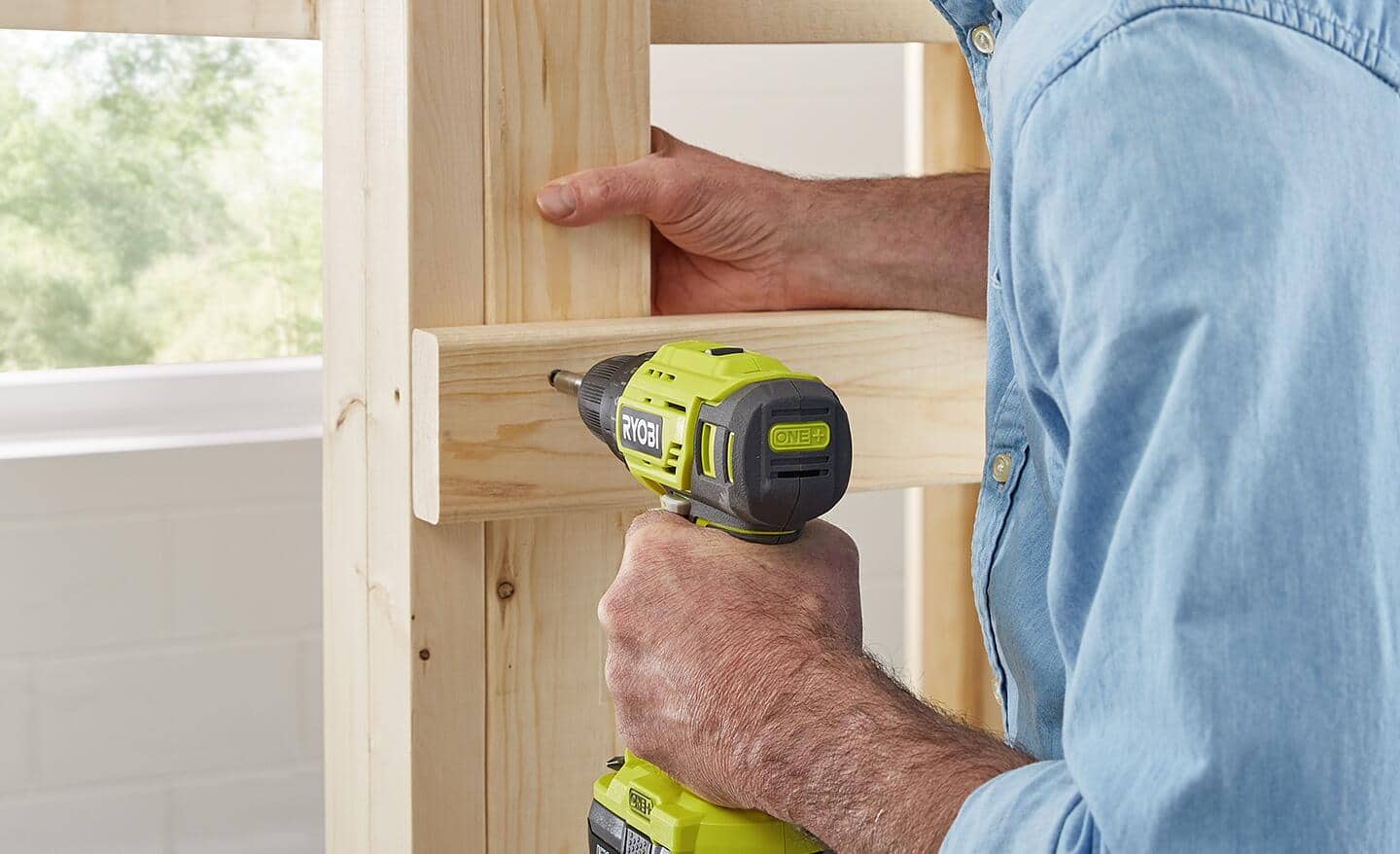 A man uses a battery power drill to drive a screw into a ladder rung on a loft bed. A man uses a battery power drill to drive a screw into a ladder rung on a loft bed.