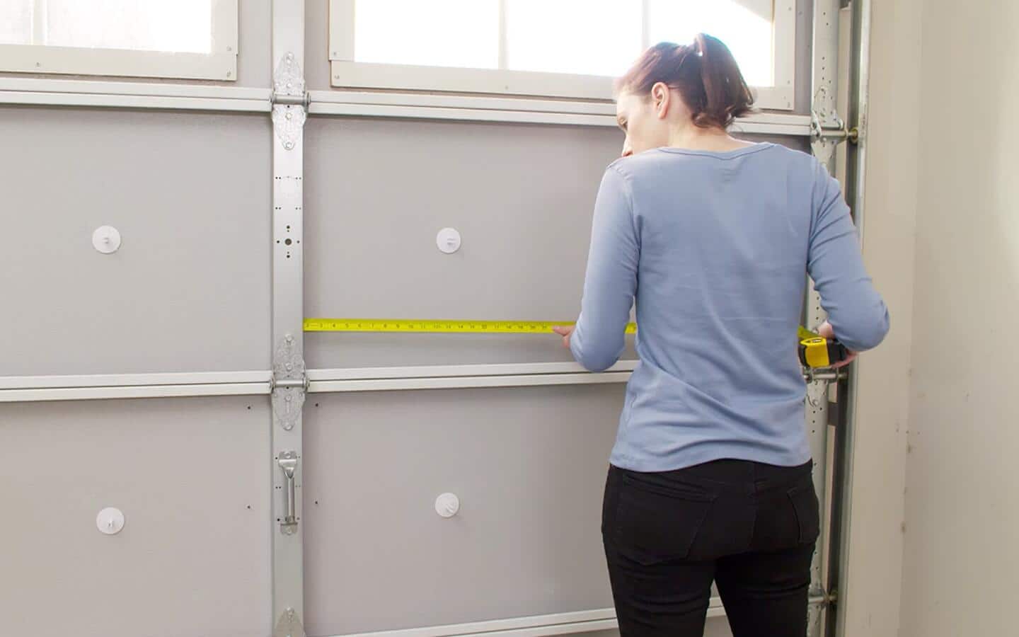 A person measuring the length of a garage door panel.