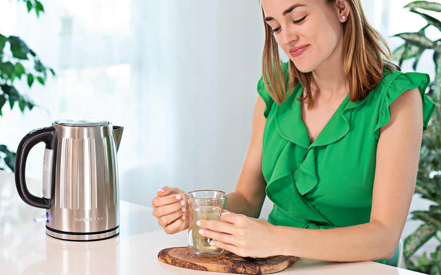 A kettle sitting on a table next to a person holding a cup of tea.