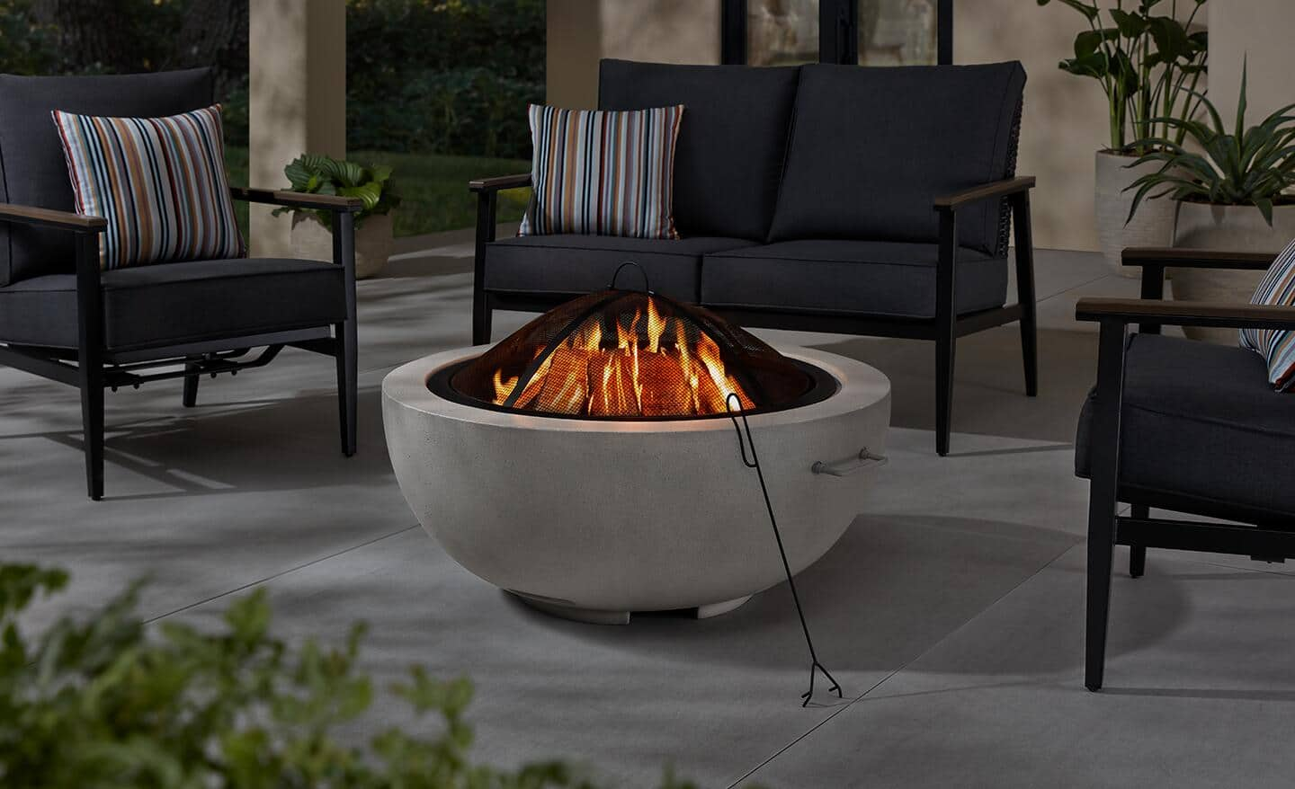 A round fire pit surrounded by chairs on a backyard patio