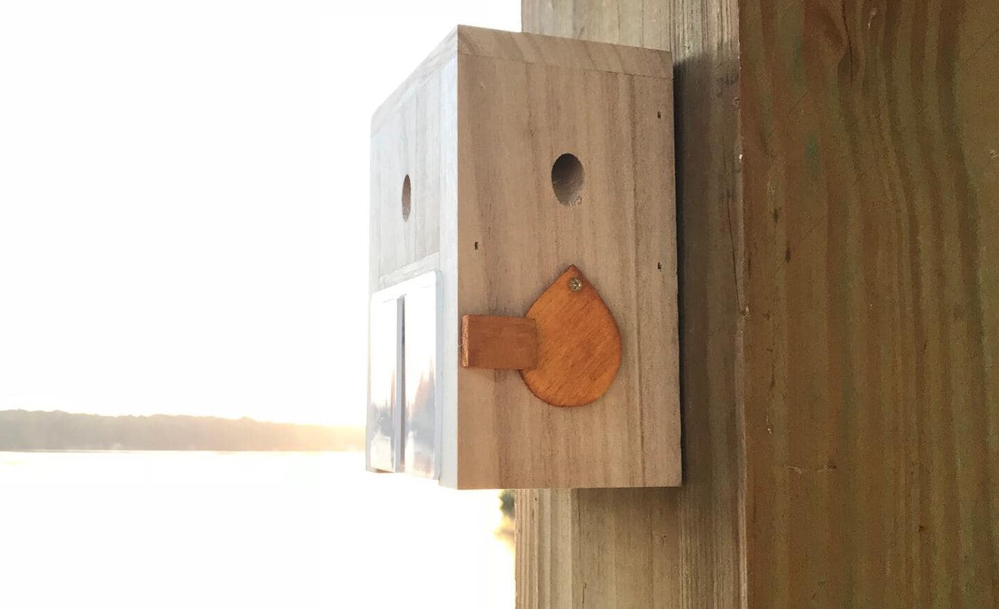 A carpenter bee trap hangs from a wooden rafter.
