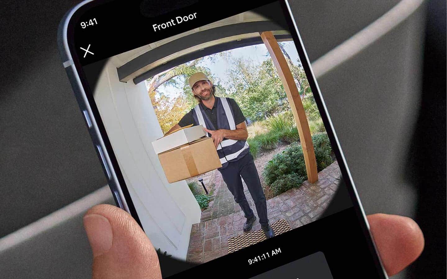 A home security camera app open on a handheld smartphone showing a delivery man with packages.