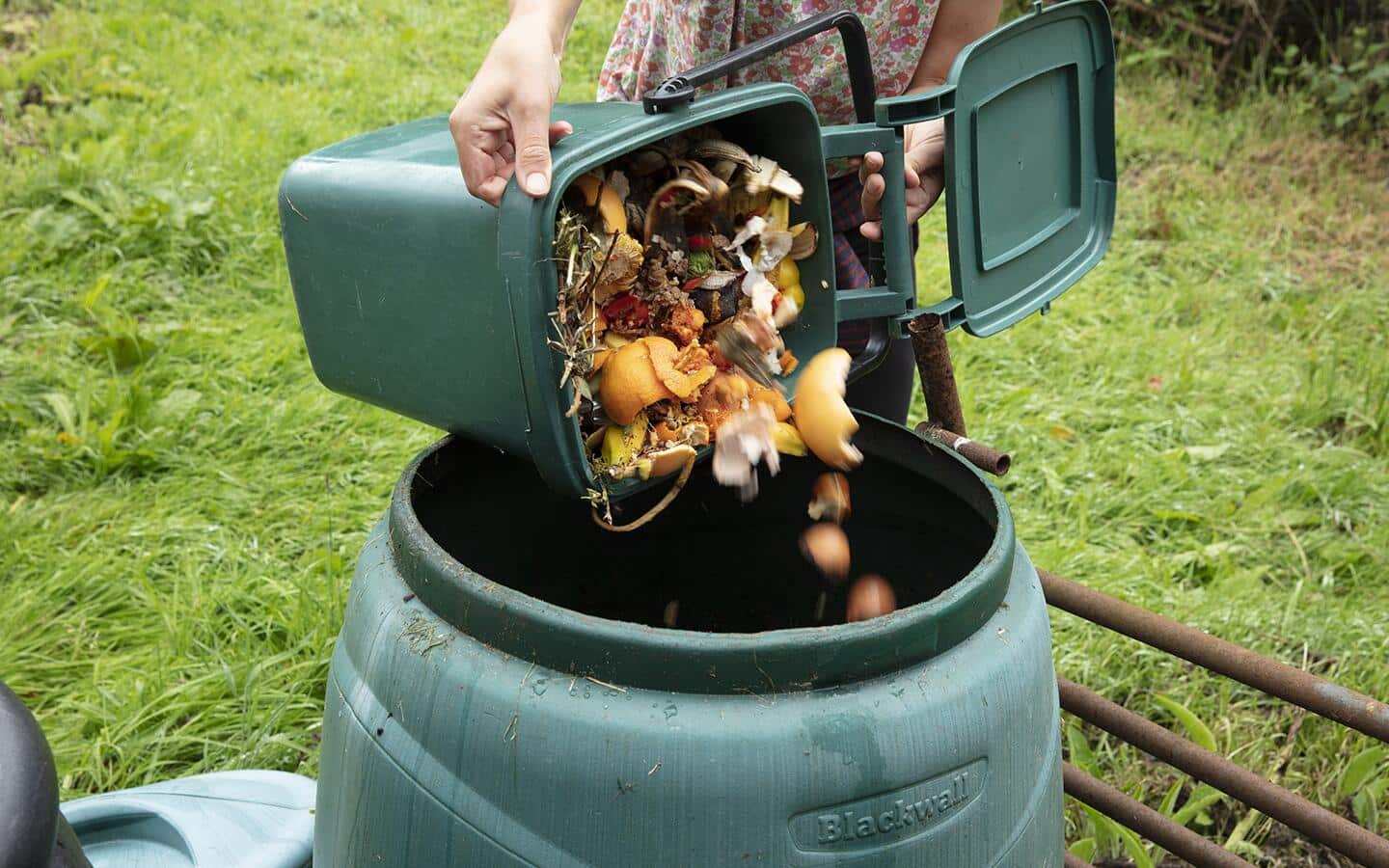 Someone emptying food waste into a green composter to make compost lasagna.