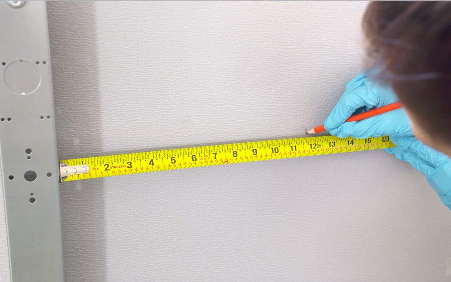A person marking a garage door panel at the 12-inch measurement on a steel measuring tape.