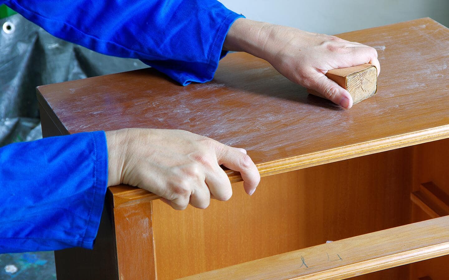 A person uses a sanding block on a wood surface.