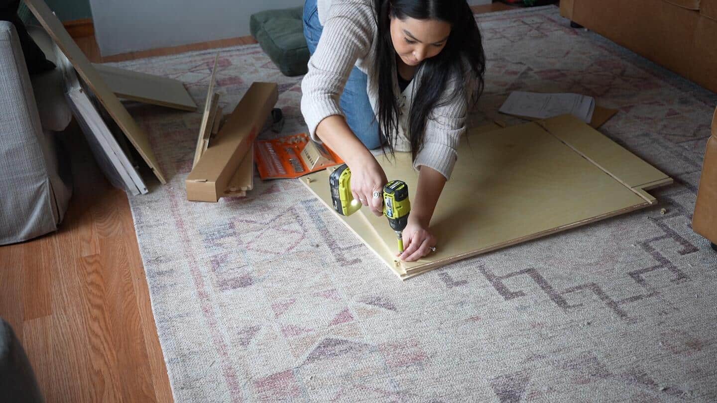 Vanessa assembles the new cabinetry on the floor, using a Ryobi handheld power tool in her assembly process.