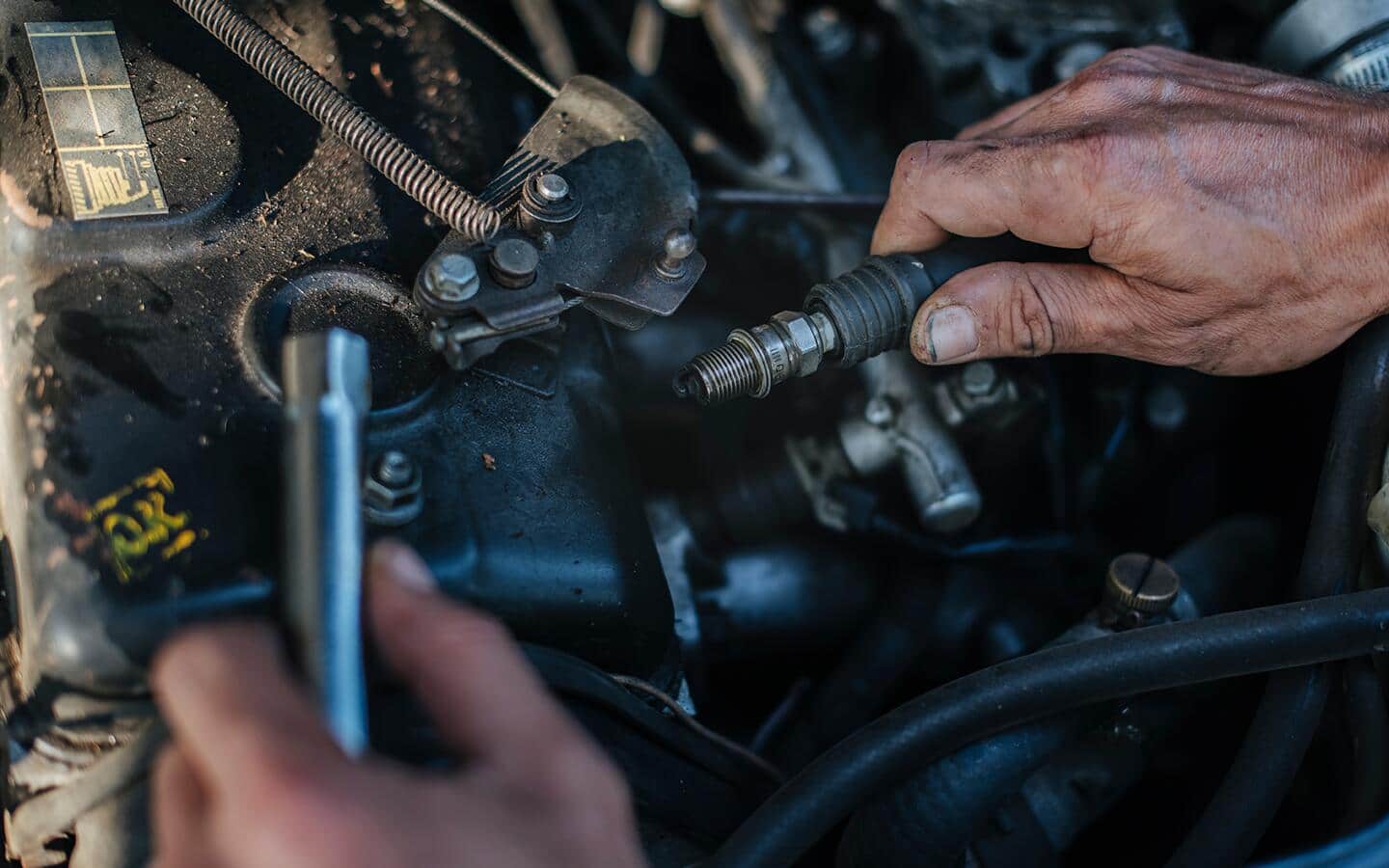 A person works underneath a car hood.