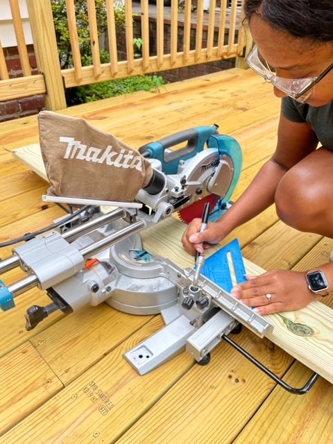 A woman marking cuts on a piece of lumber resting on a Makita miter saw.
