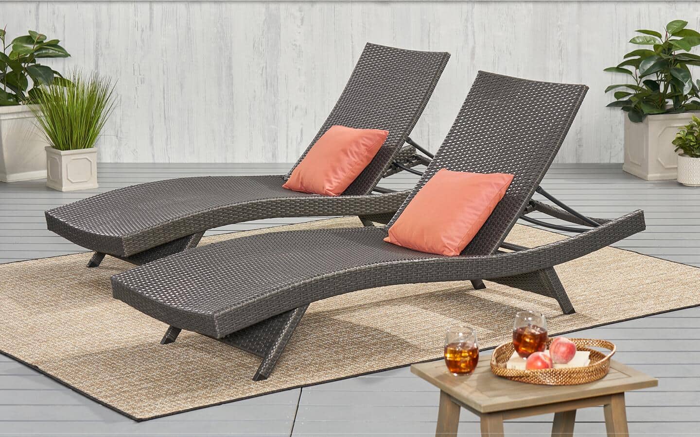 Side-by-side brown lounge chairs with orange pillows on a tan outdoor patio rug.
