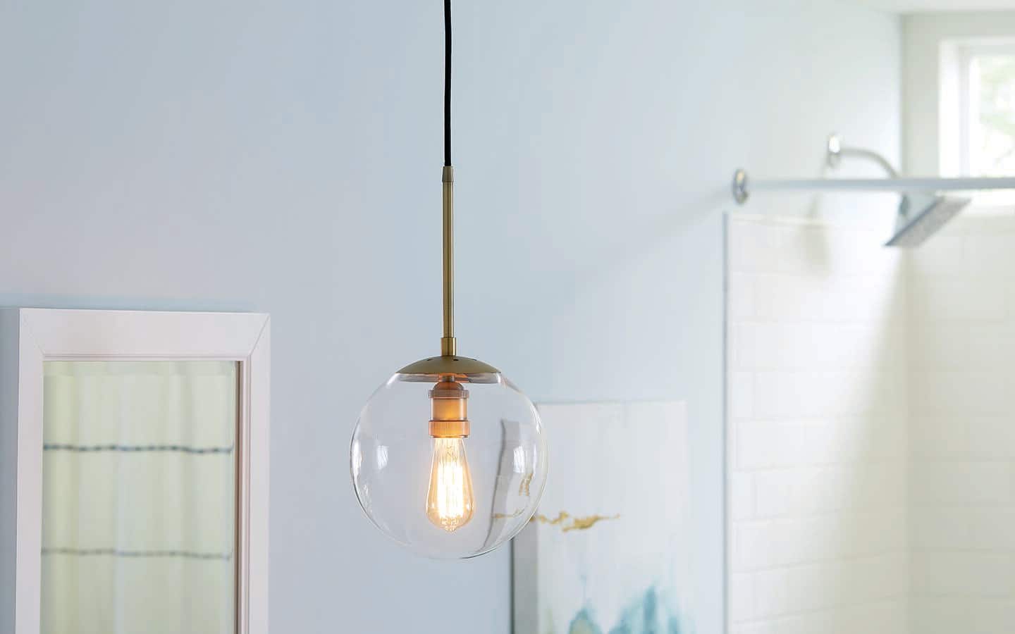 A pendant light with a clear glass globe hangs from the ceiling of a bathroom. A pendant light with a clear glass globe hangs from the ceiling of a bathroom.