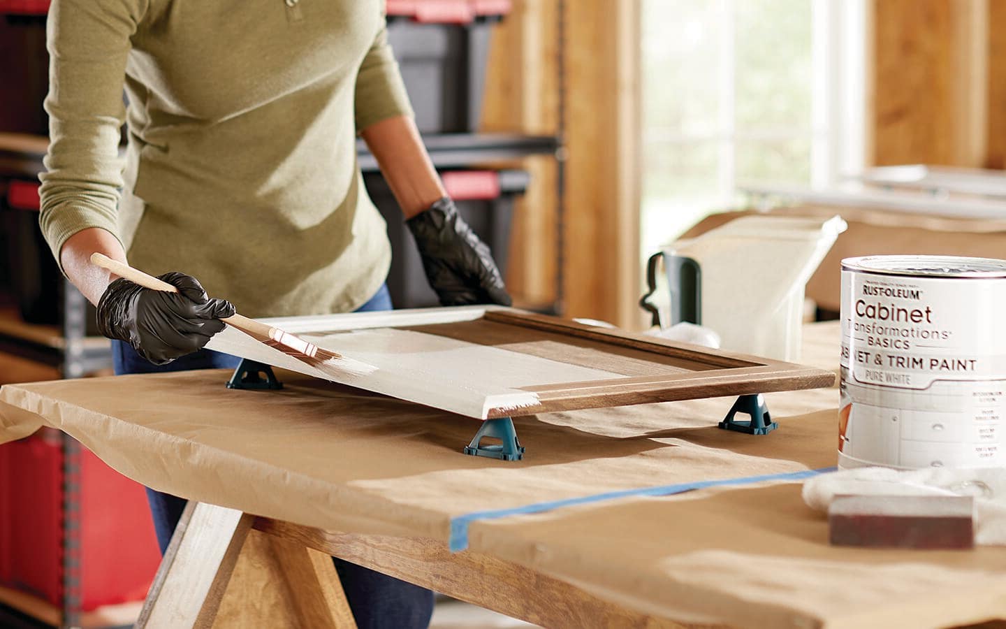 A gloved individual applies white paint to a cabinet door. A gloved individual applies white paint to a cabinet door.