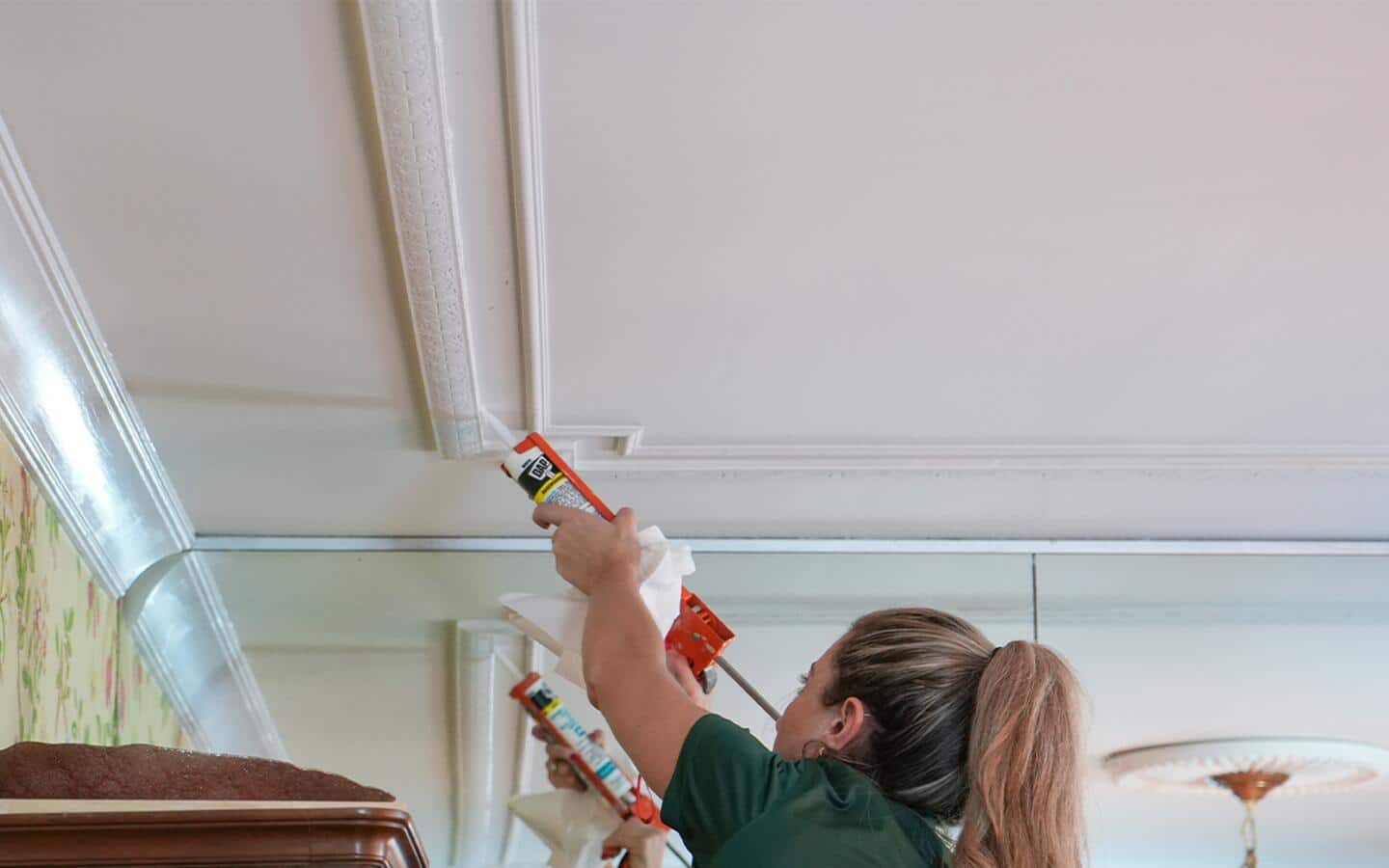 A person using a caulk gun to apply caulk to ceiling moulding. 
