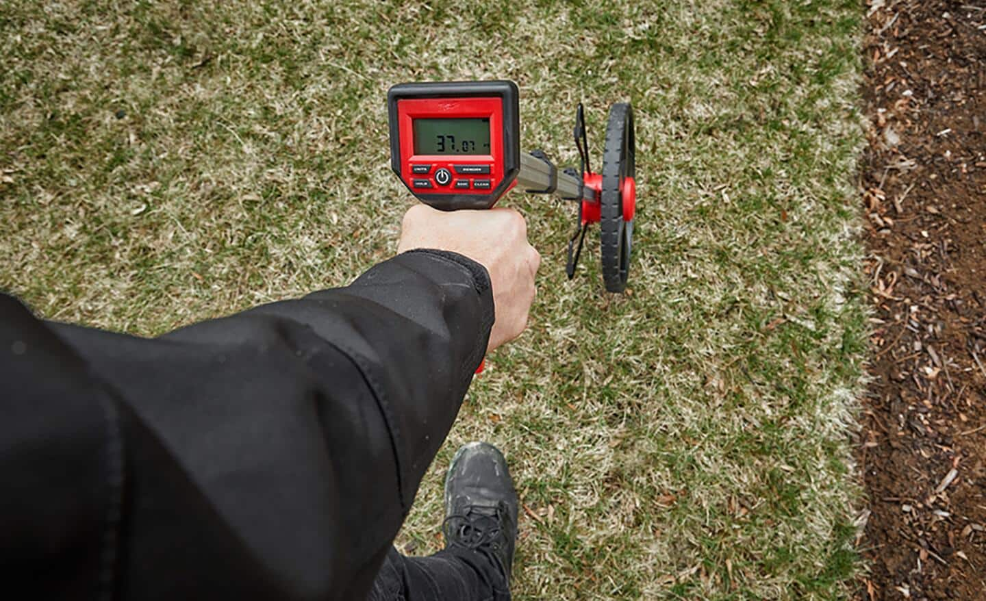 Someone measures a bare yard for sod with a measuring wheel.