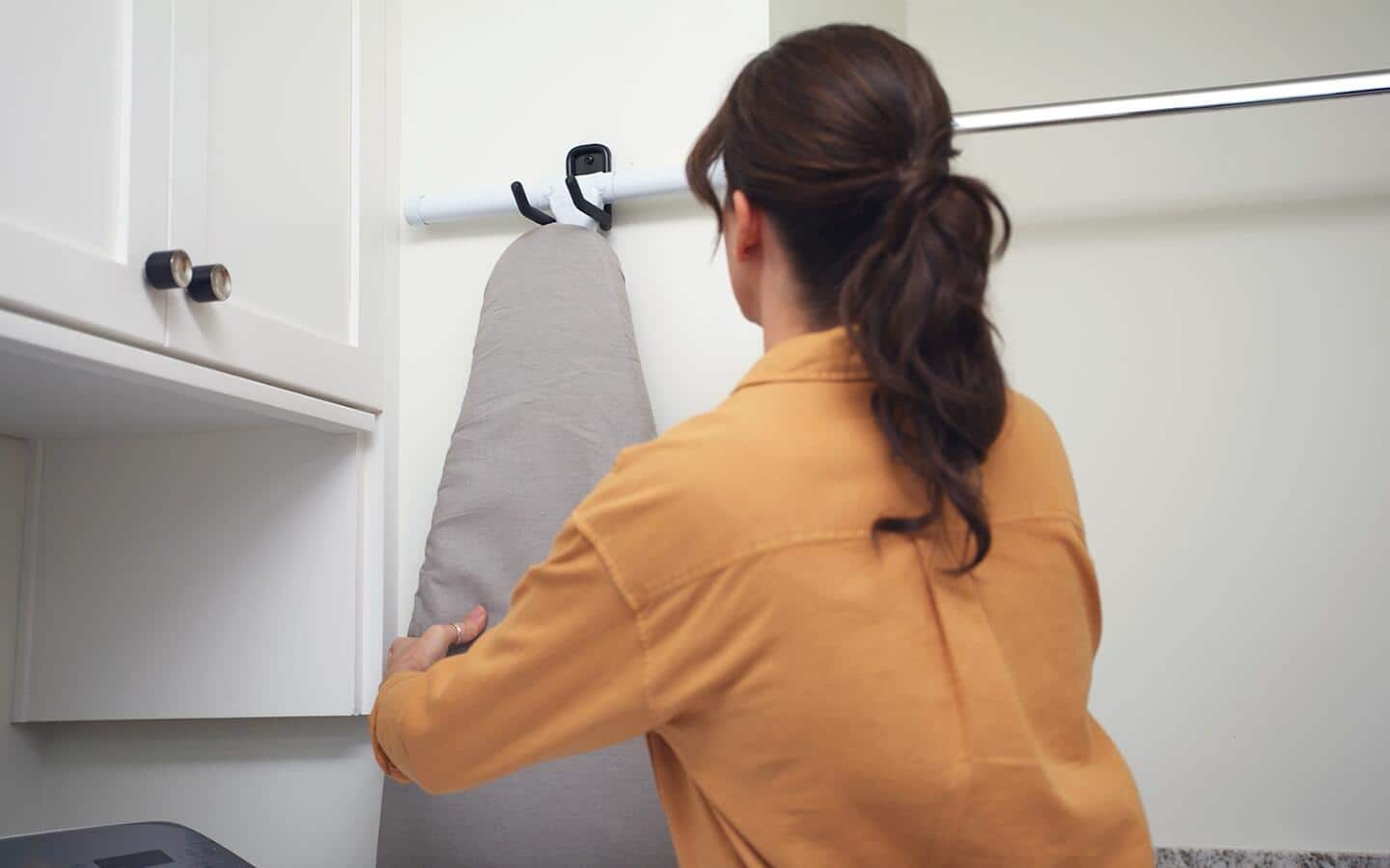 A woman hanging an ironing board on the wall. A woman hanging an ironing board on the wall.