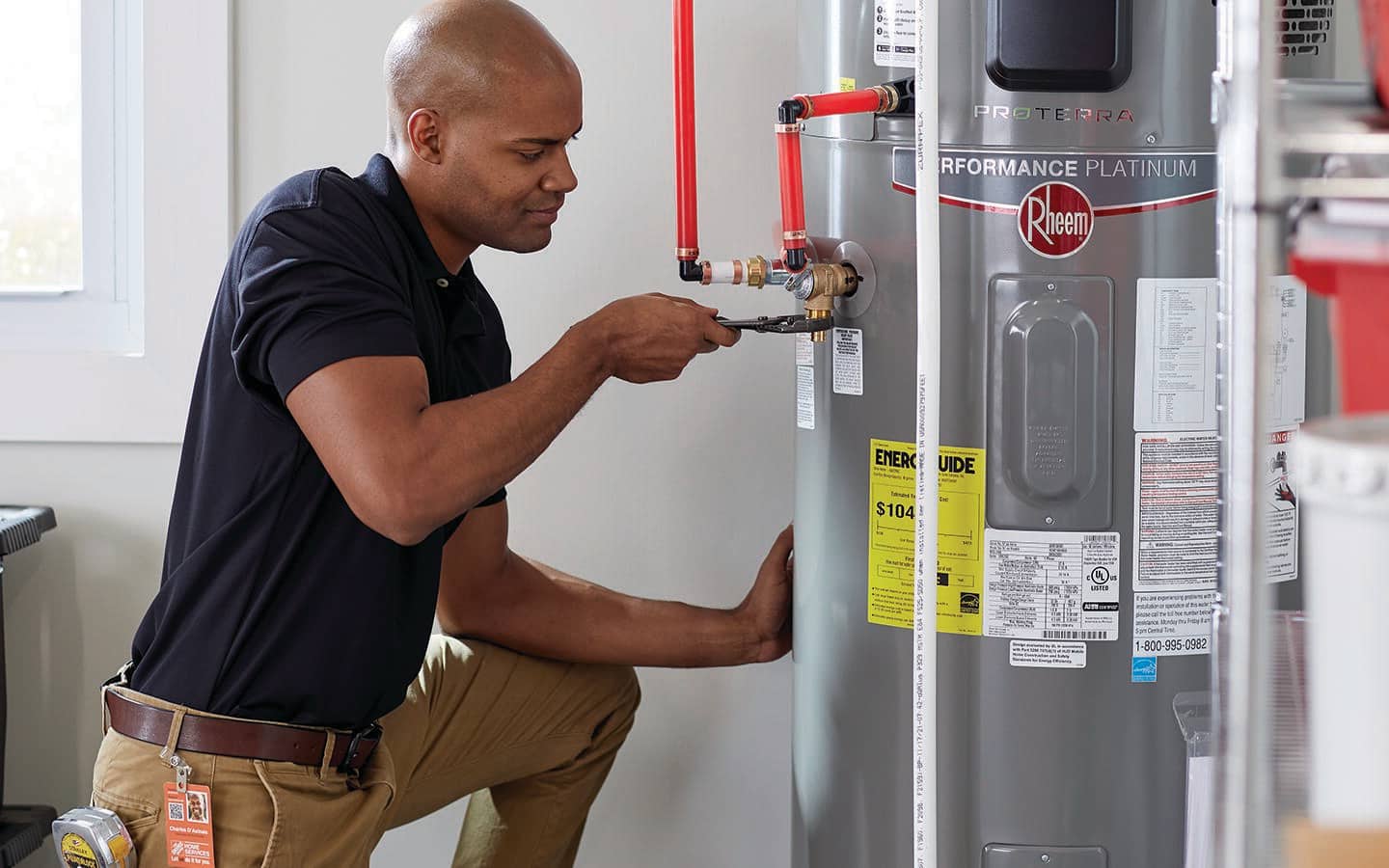 A man uses a wrench to adjust a water heater inside a home. 