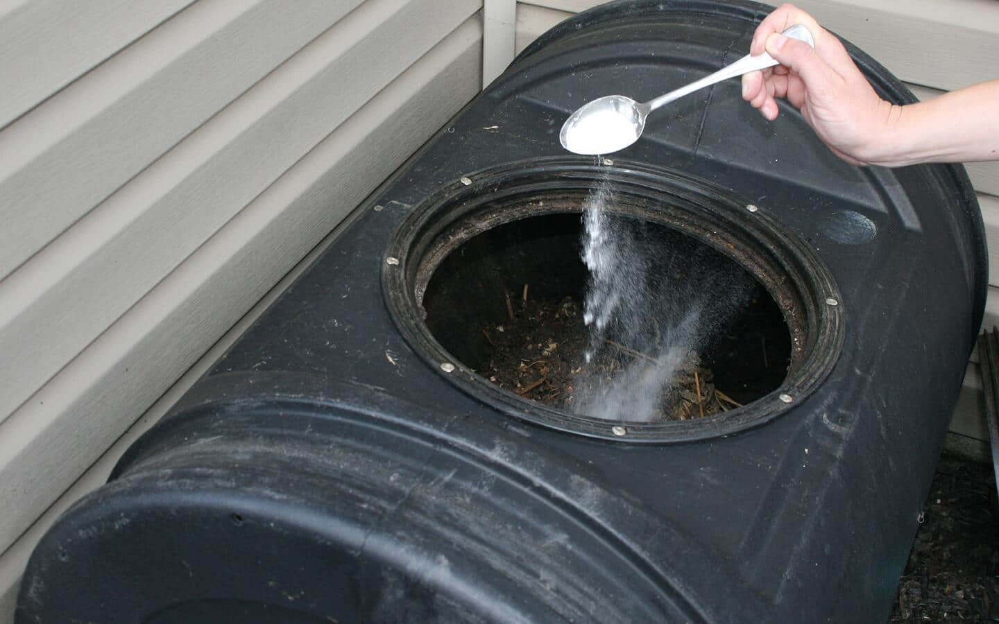 A person spooning compost starter into a black composter.