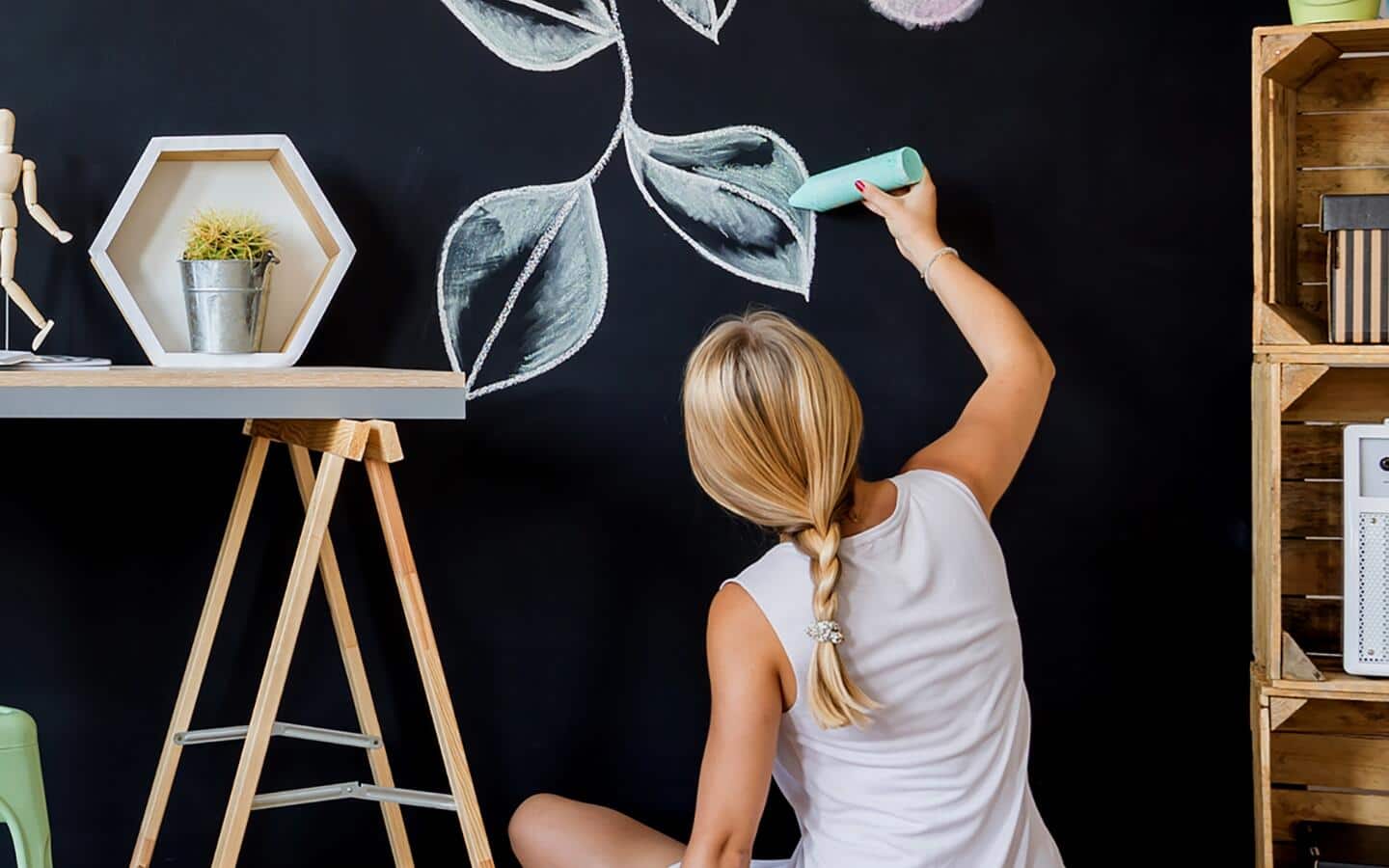 Someone drawing a leaf on a wall with green chalk.