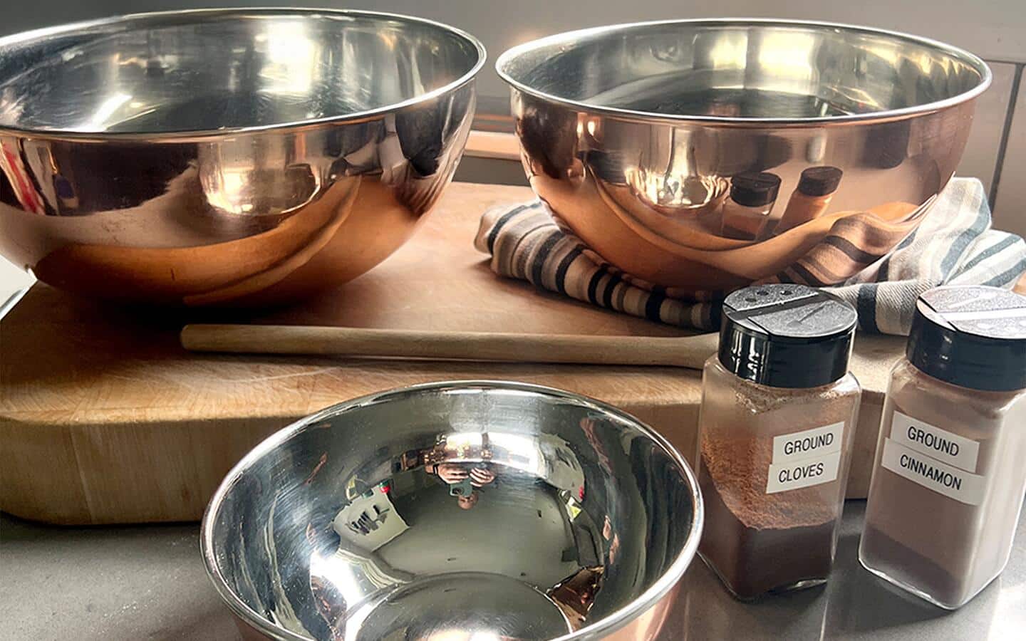 Three copper mixing bowls placed on a kitchen counter with ingredients for a recipe.