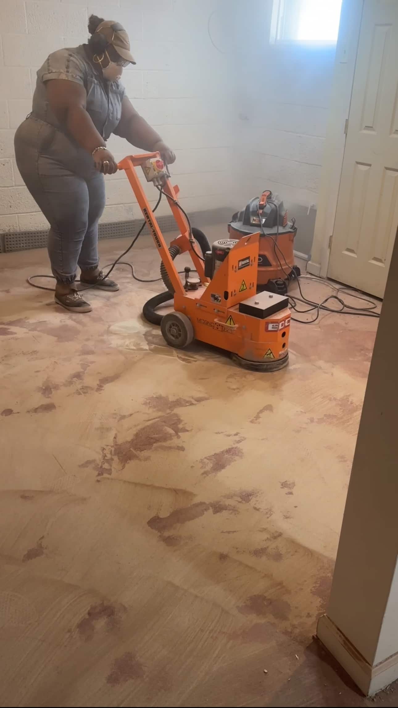 A woman using a concrete grinder over a recently demo’d floor.