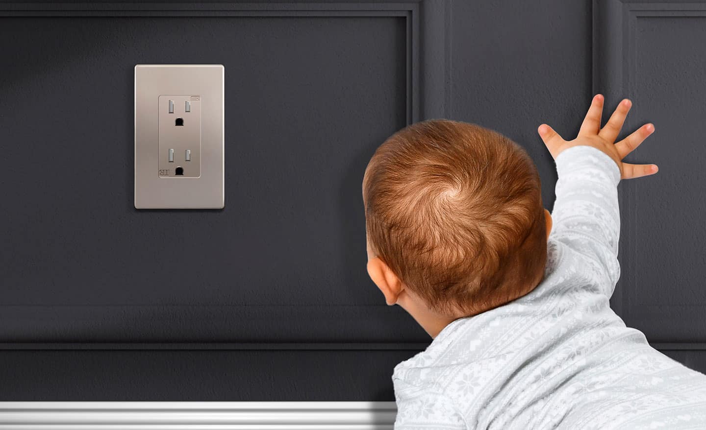 A baby crawling up to a tamper-resistant receptacle on a wall.