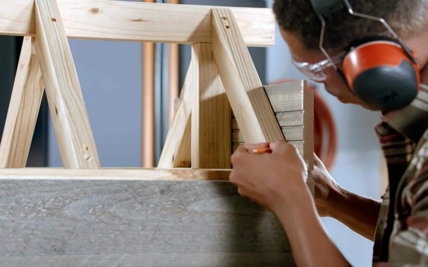 A person in headphones takes measurements of a dog house's siding.
