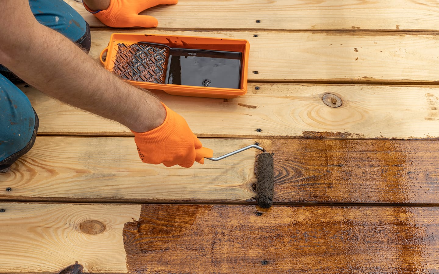 Person uses a roller to apply wood stain to a deck