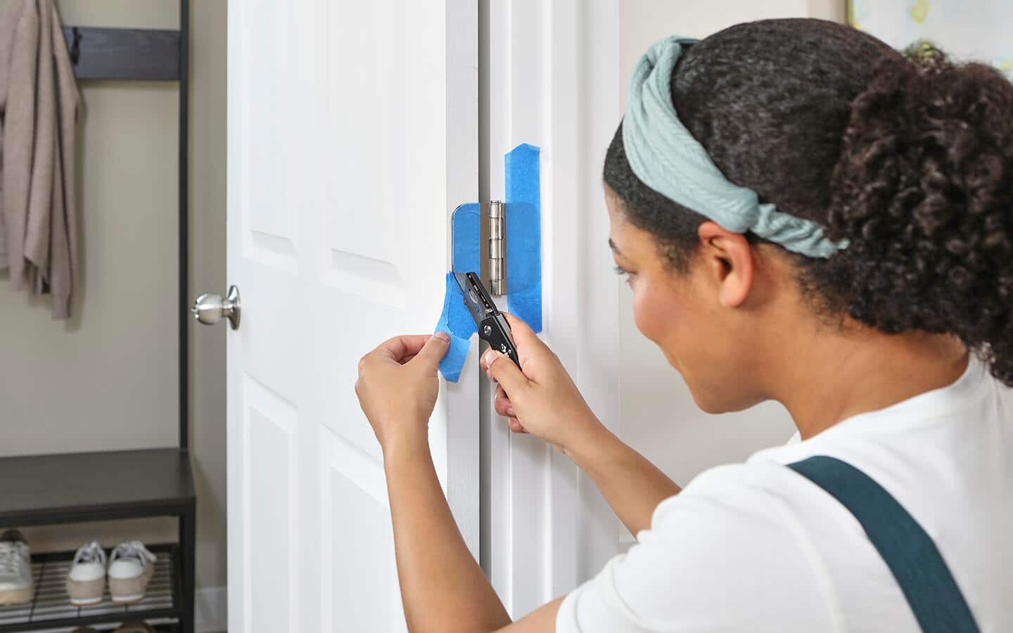 Door hinges are covered with blue painter's tape and the tape is being trimmed with a utility knife. Door hinges are covered with blue painter's tape and the tape is being trimmed with a utility knife.