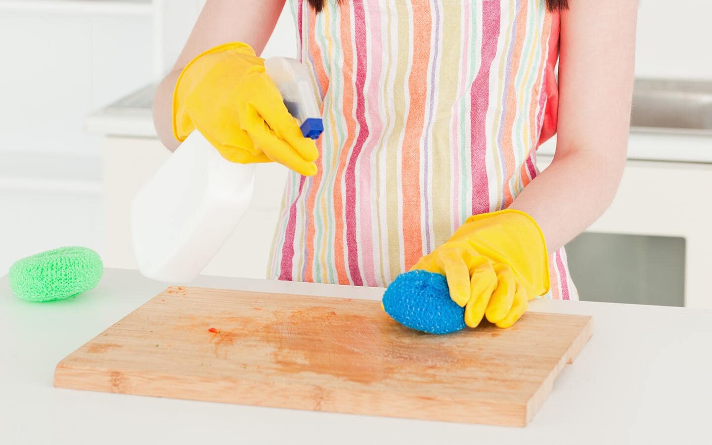 A woman in a kitchen sprays a stained wooden cutting board with cleaner. A woman in a kitchen sprays a stained wooden cutting board with cleaner.