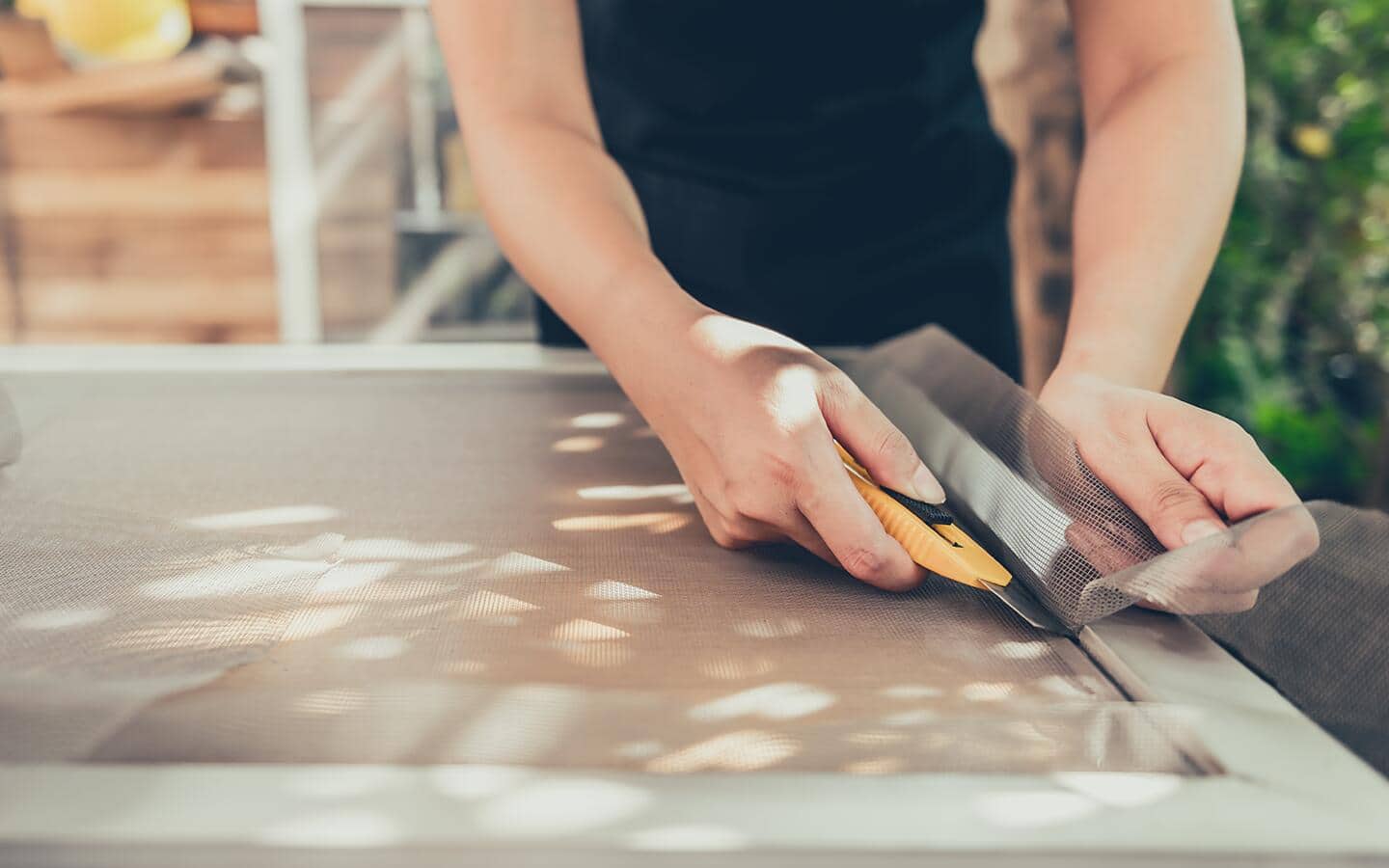 A person using a utility knife to cut away excess screen fabric. A person using a utility knife to cut away excess screen fabric.