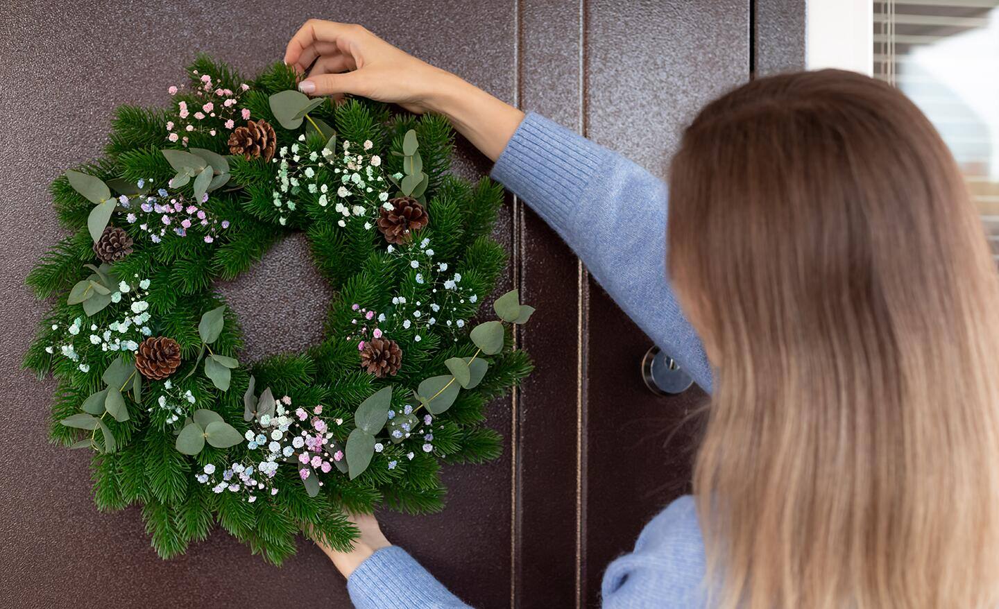 A woman hangs a wreath on a front door. A woman hangs a wreath on a front door.
