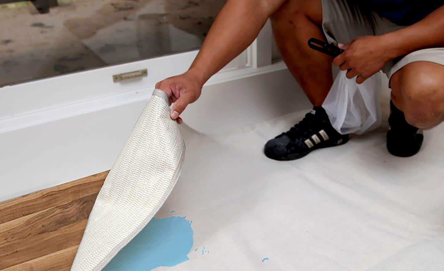 A drop cloth with spilled blue paint being lifted off of the floor.