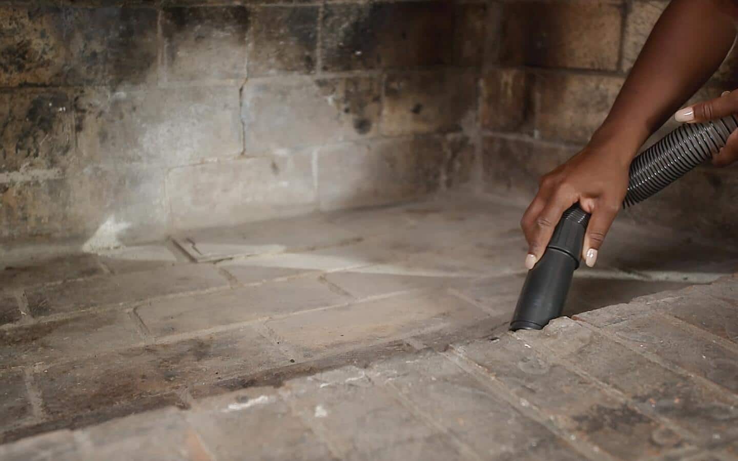 A person uses a vacuum hose to clean dirt from a fireplace.