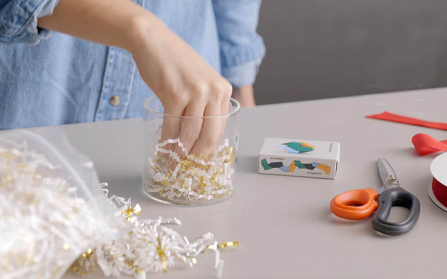 White- and gold-colored shredded paper is placed in a glass canister.