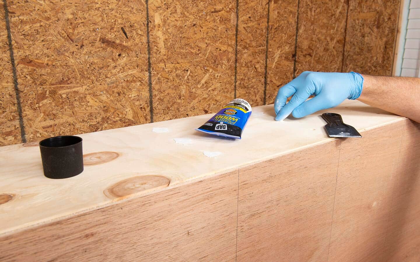 Wood filler is used to fill and cover screws on the side of a shelving unit under construction.