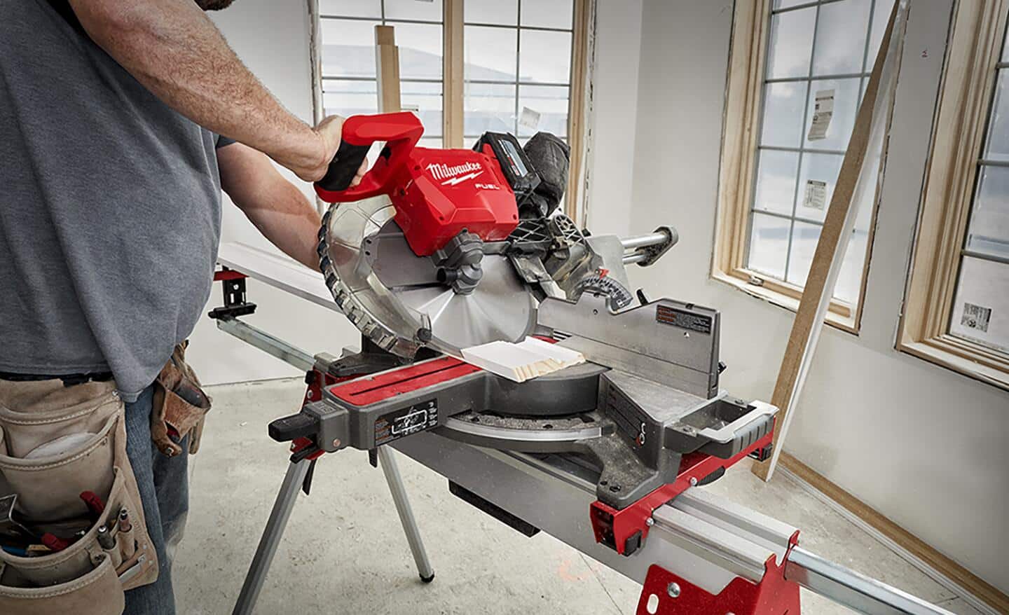 A person tilts a miter saw at an angle to make a bevel cut on a board.